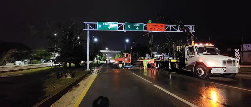 De noche, la grúa articulada termina de montar un marco elevado con los tableros «Progreso» y «Motul» sobre una vía de dos carriles