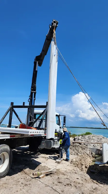 El brazo de la grúa articulada extendido hacia arriba sostiene un elemento largo de concreto en posición vertical