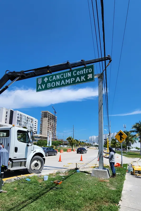 La grúa articulada coloca una señal informativa «Cancún Centro · Av. Bonampak» sobre su poste, a un lado de la avenida